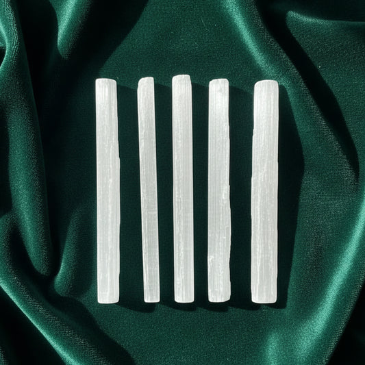 Five rough selenite bars laid side by side on green satin, each an unpolished fibrous white crystal with a satin sheen.
