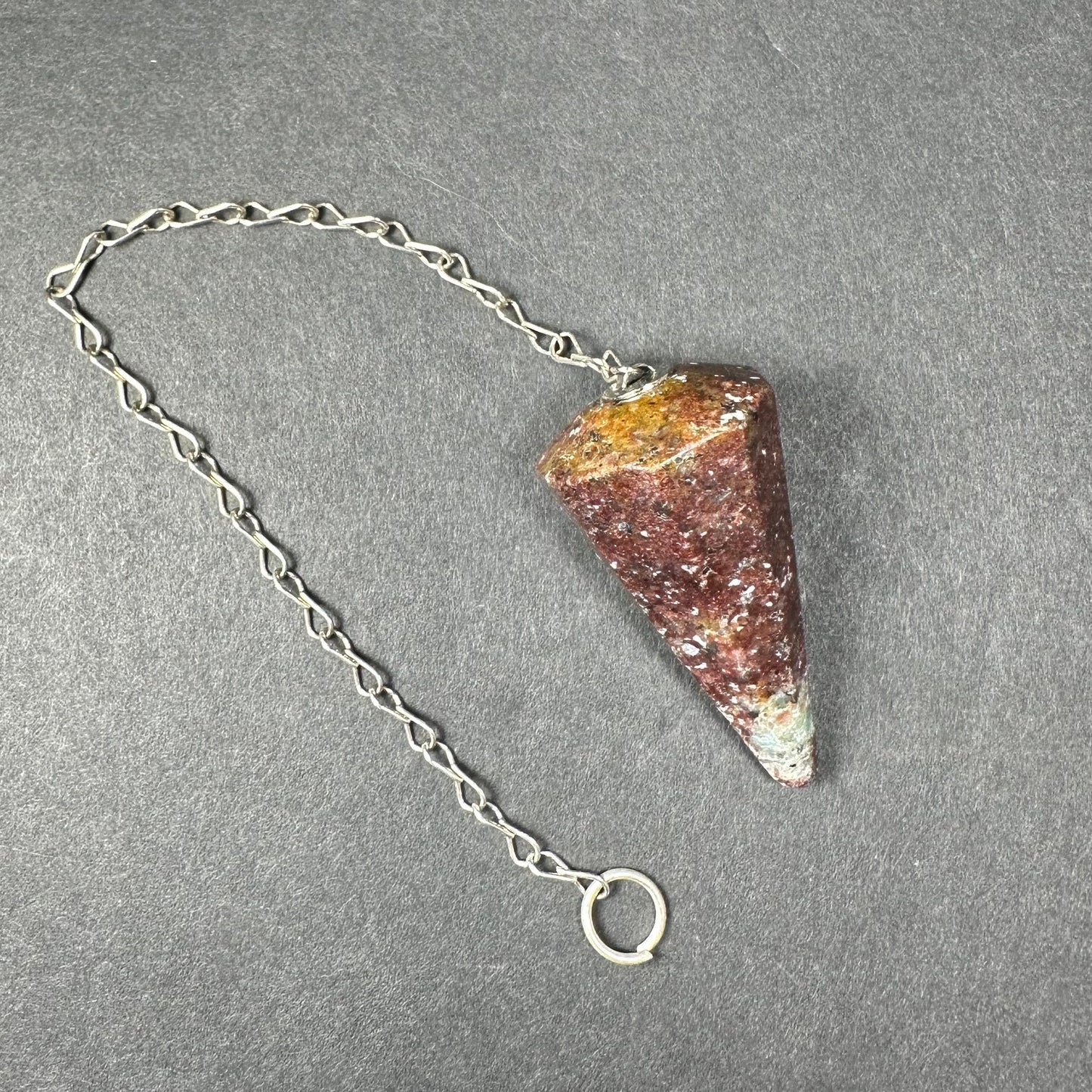 Faceted stone pendulum hanging from a seven-inch metal chain against a dark background — view 11