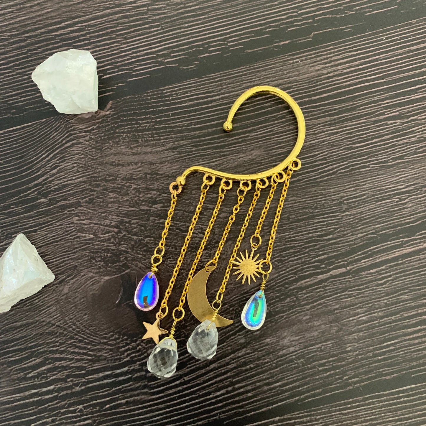 Gold ear cuff earring with sun and moon charms and a long natural quartz crystal drop, worn on one ear — product photo 2