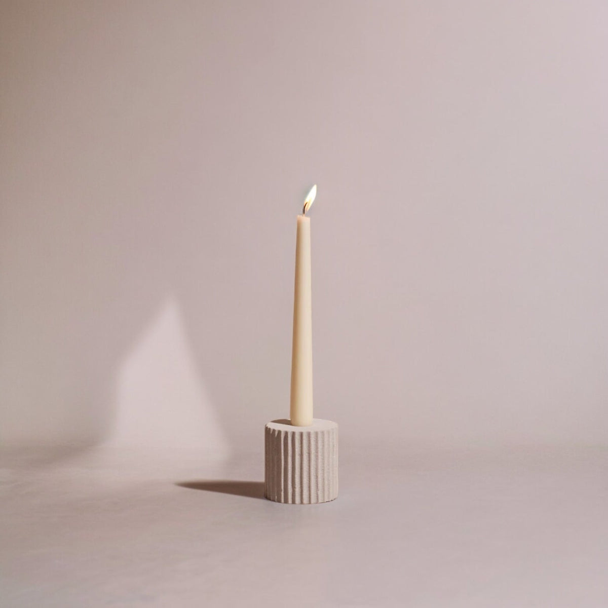Small Pilar candle holder in matte sandstone with vertical fluting, holding a lit taper