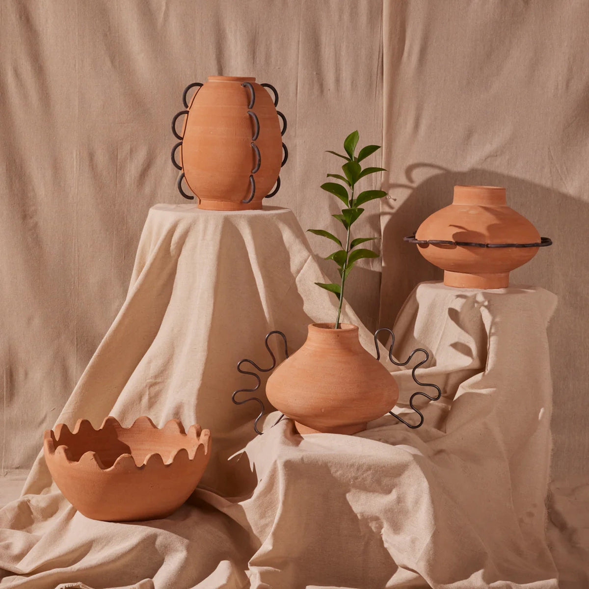 Ines vessel grouped with other terracotta pieces and a green sprig on draped linen