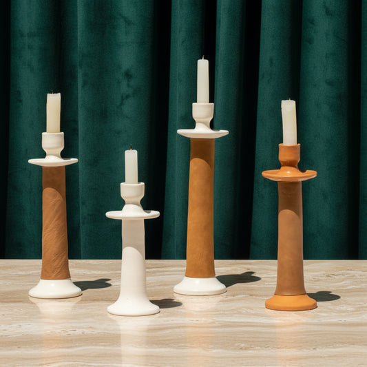 Four leather-wrapped candle holders in cream, tan and terracotta with tapers, green velvet backdrop