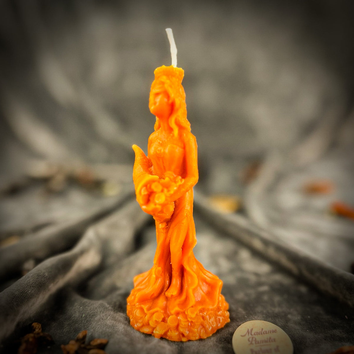 Fortuna Goddess of Luck beeswax candle in orange on draped gray fabric