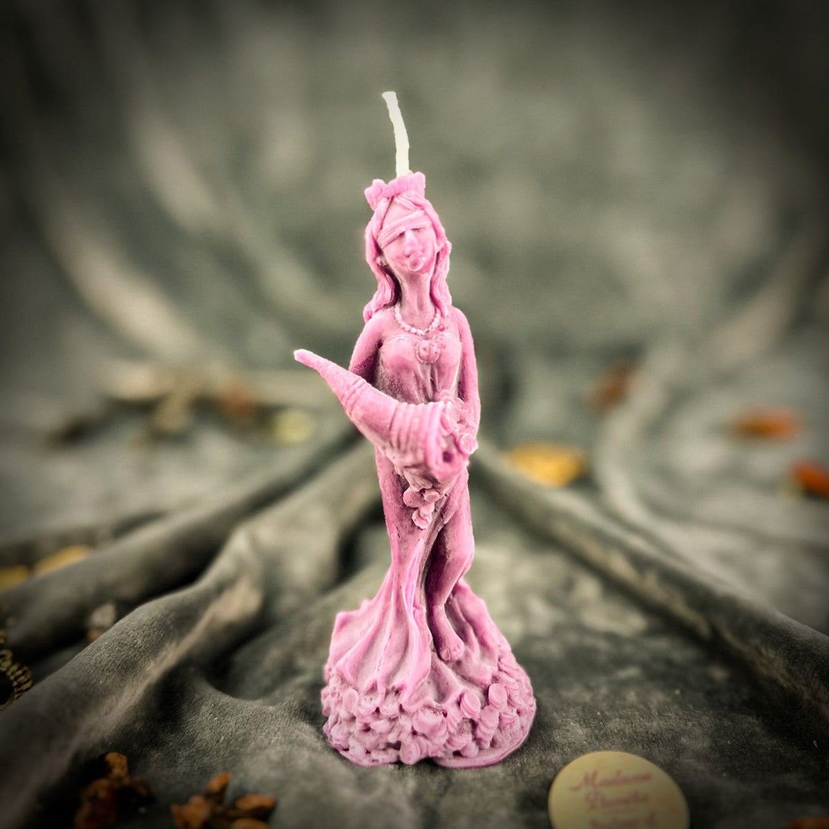 Fortuna Goddess of Luck beeswax candle in pink on draped gray fabric