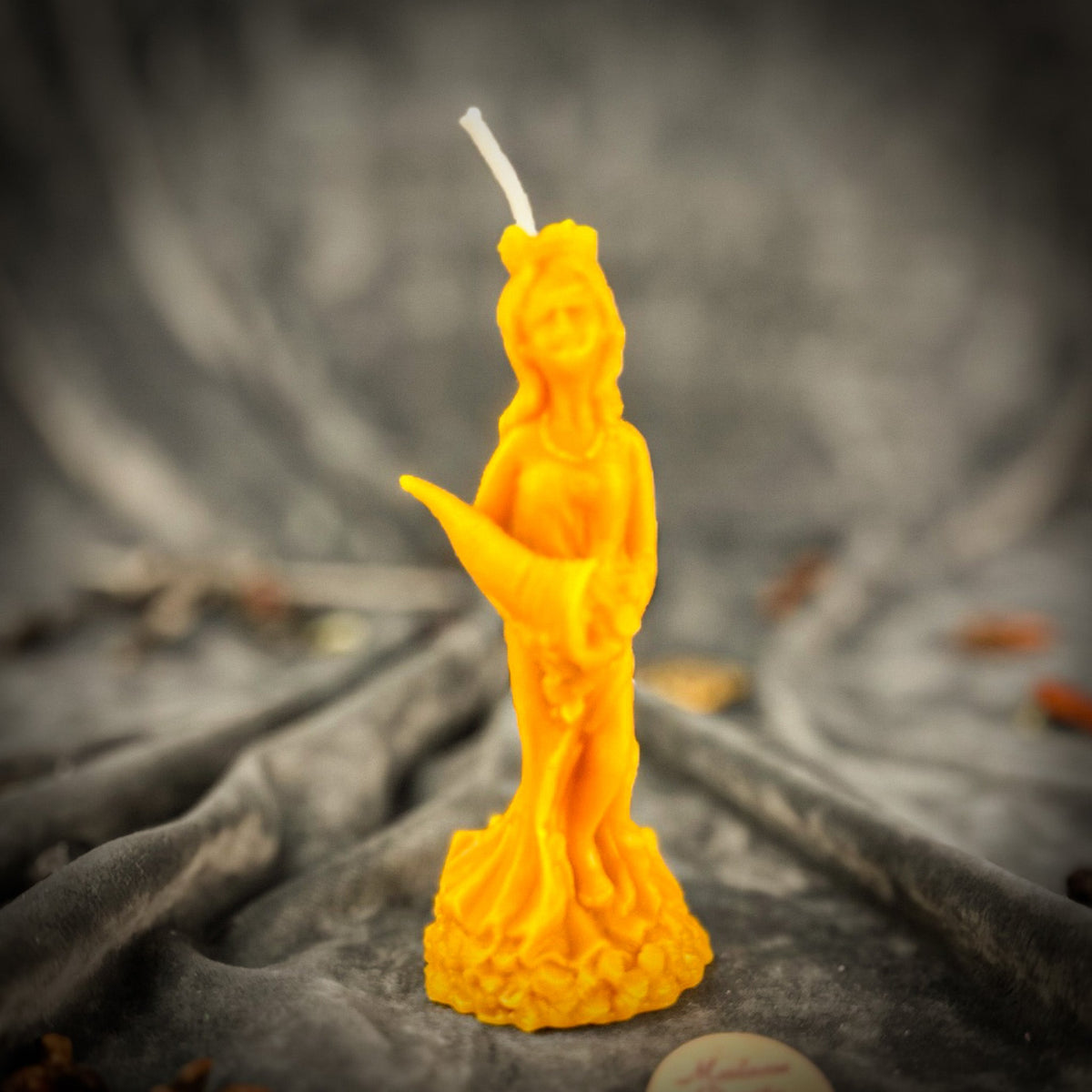 Fortuna Goddess of Luck beeswax candle in yellow on draped gray fabric