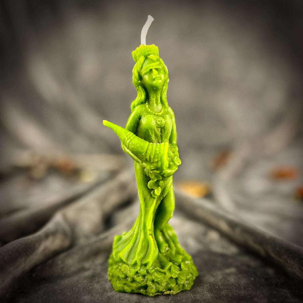Fortuna Goddess of Luck beeswax candle in green on draped gray fabric