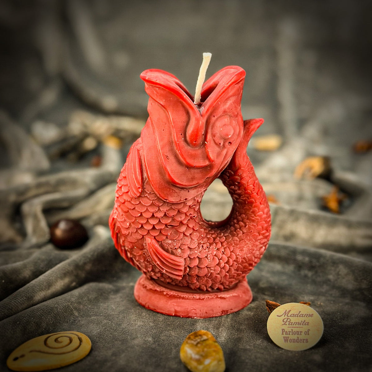 Red fish-shaped candle on gray velvet with whole star anise scattered around its base