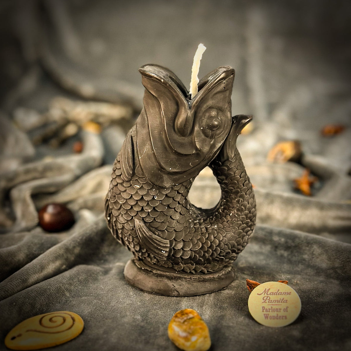 Charcoal gray fish-shaped candle on gray velvet with the Parlour of Wonders token in front