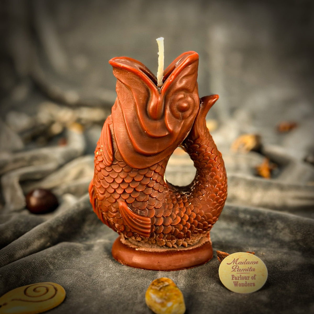 Copper-brown fish-shaped candle on gray velvet, scales and fins picked out with a metallic finish