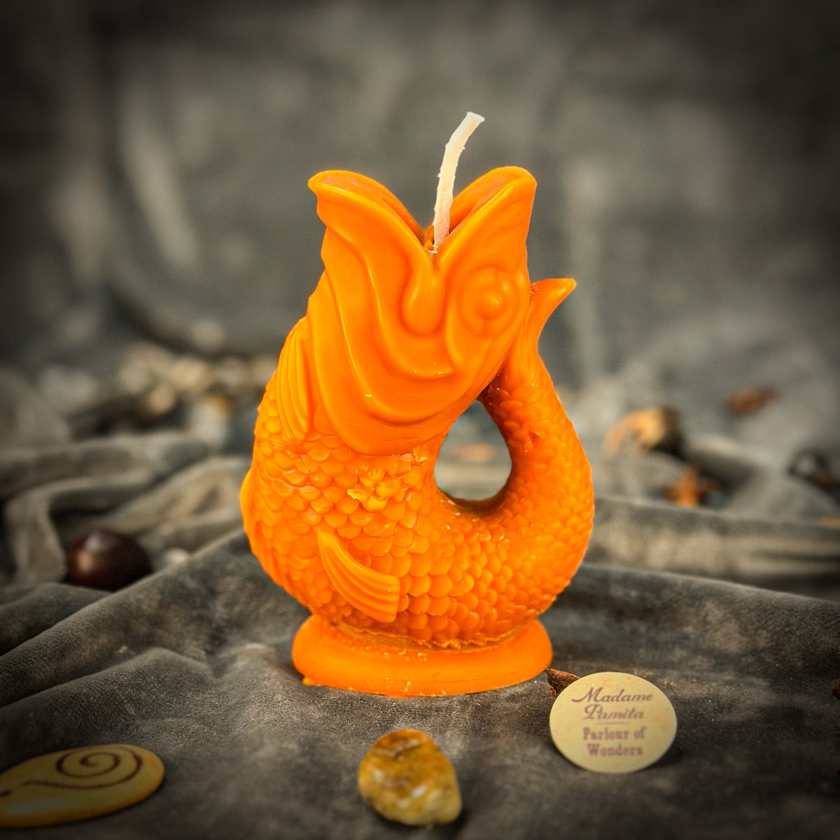 Bright orange fish-shaped candle on gray velvet, its round base resting in the folds of the fabric