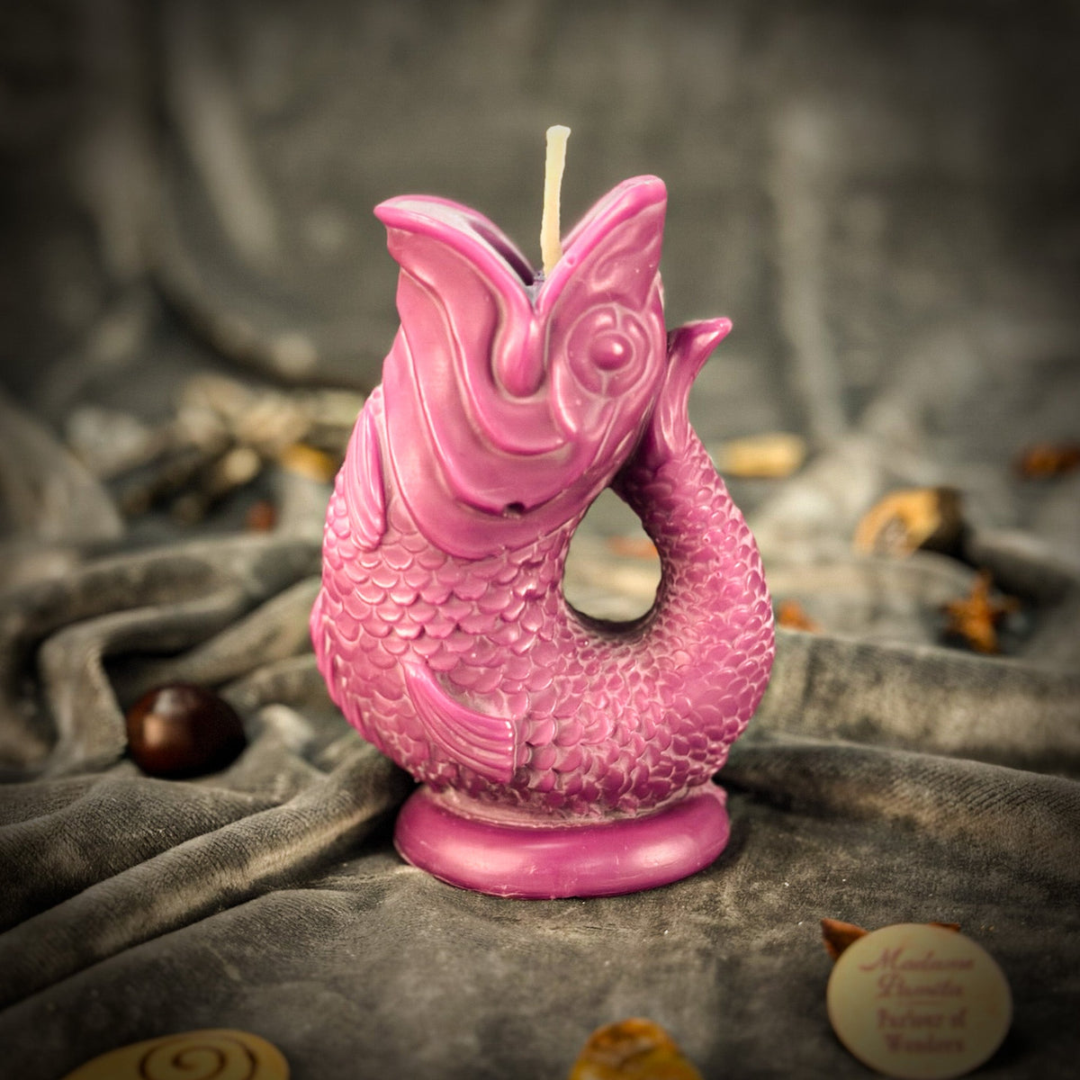 Magenta fish-shaped candle on gray velvet, the tail curving round to meet the head