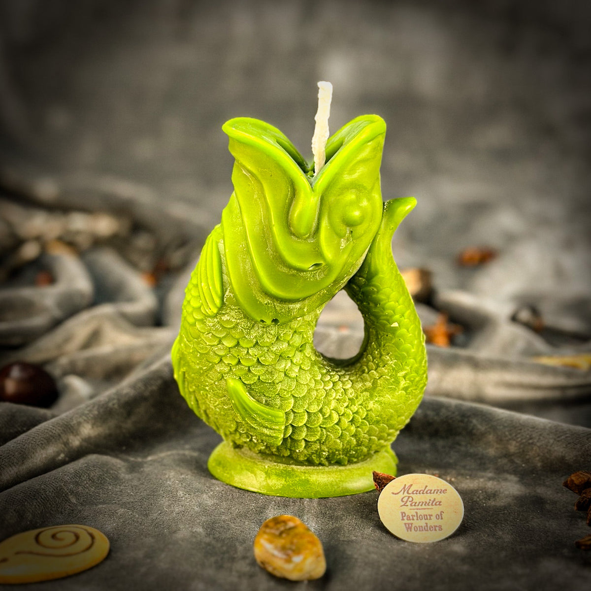 Lime green fish-shaped candle on gray velvet, its molded scales and curved tail forming an open loop