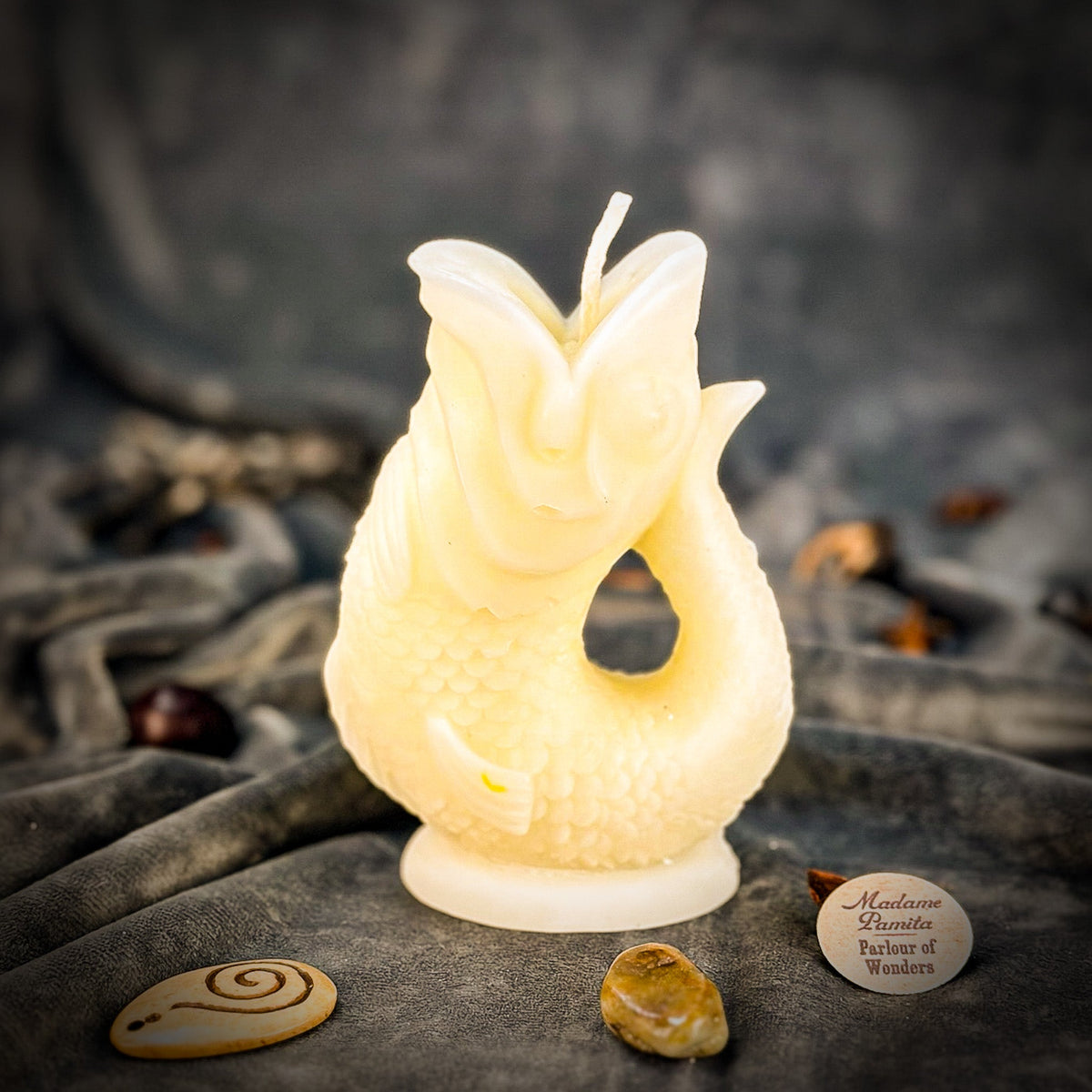 Cream fish-shaped candle on gray velvet, the scale texture visible along the body in soft light