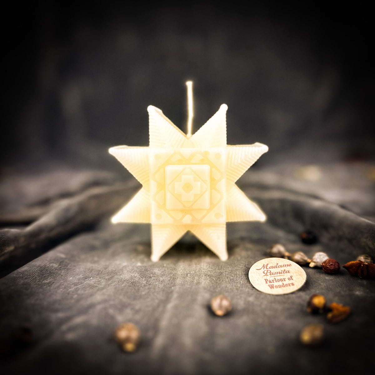 Ivory Ruzha star candle standing on gray velvet with the maker's tag and loose herbs
