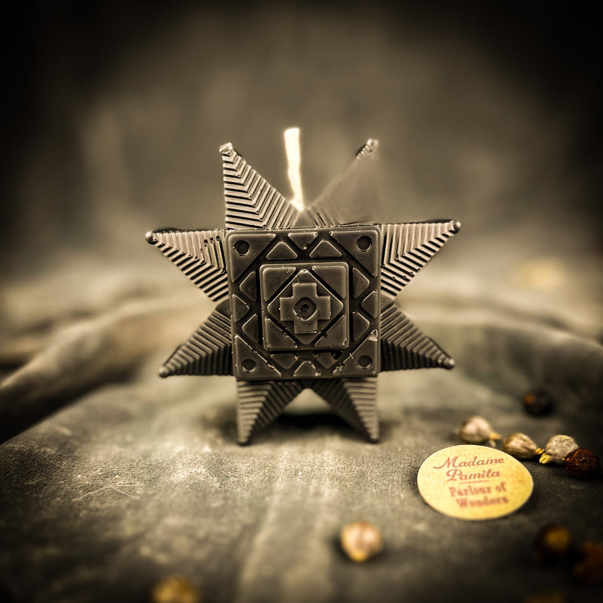 Black Ruzha star candle on gray velvet, the pressed rosette pattern picked out in shadow