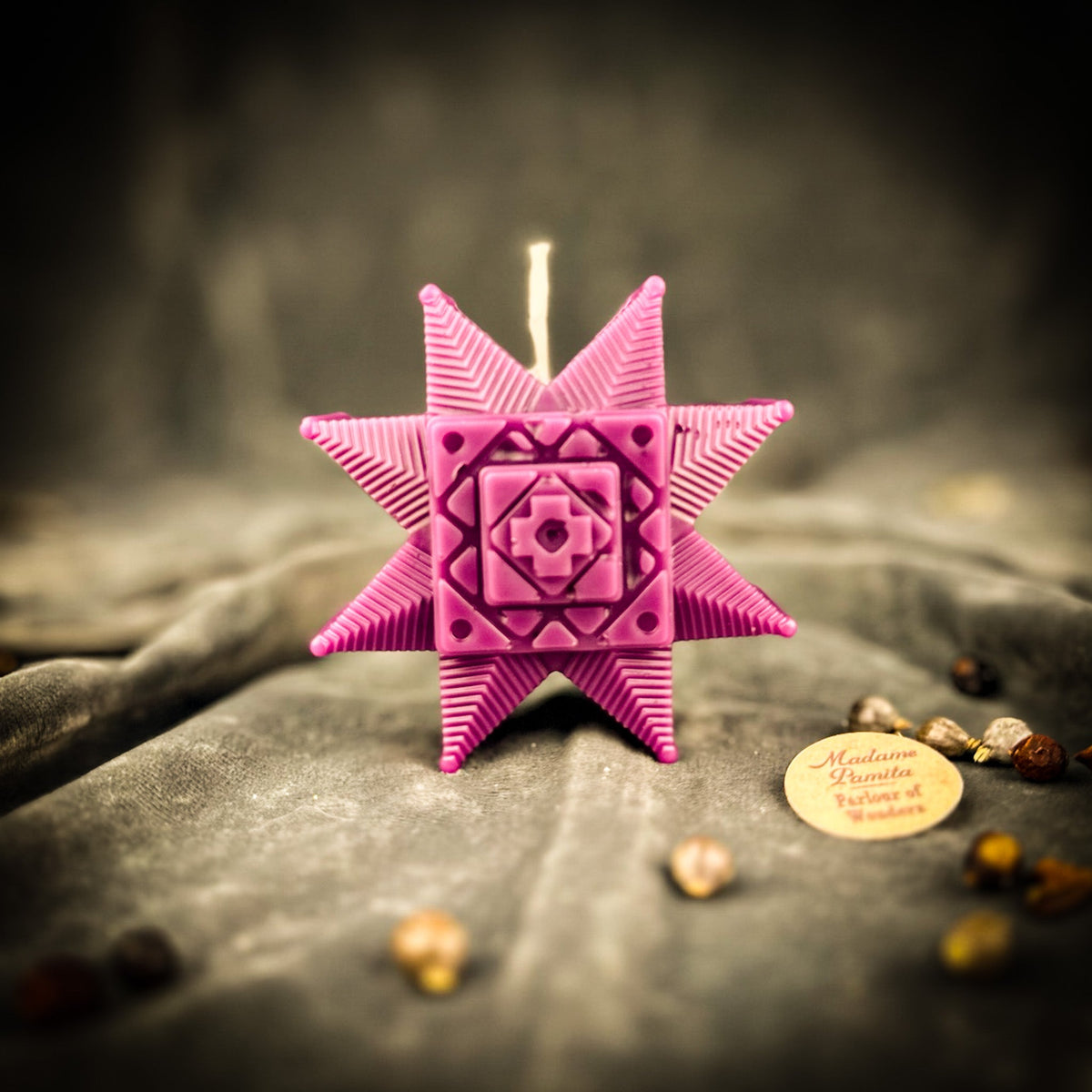 Magenta Ruzha star candle standing on gray velvet
