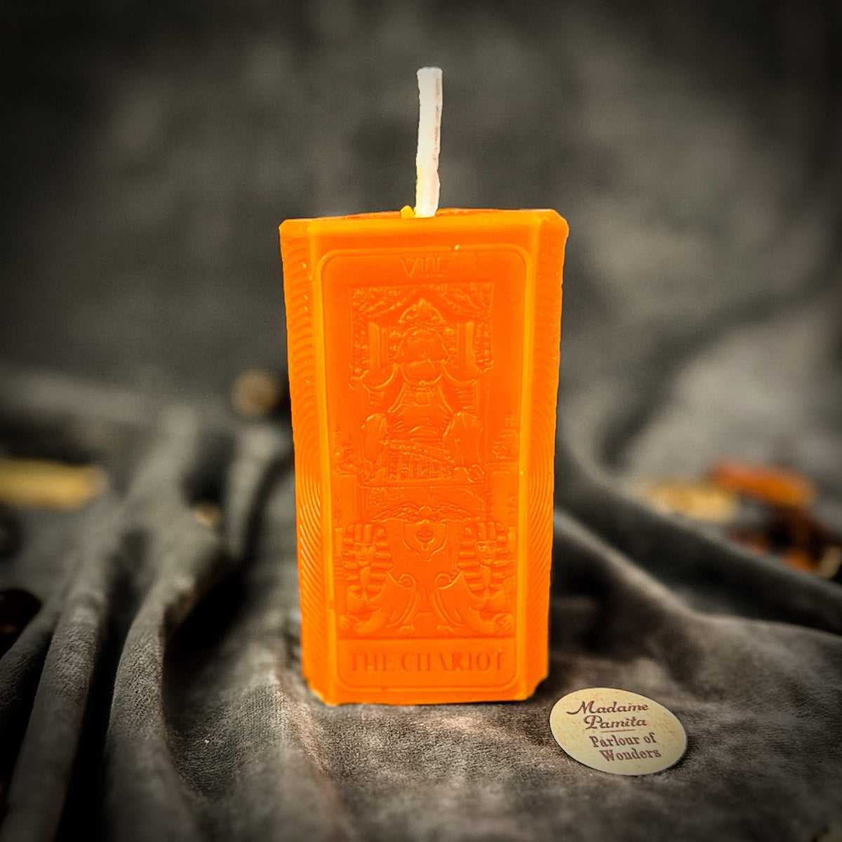 Bright orange beeswax The Chariot tarot card candle on draped gray fabric