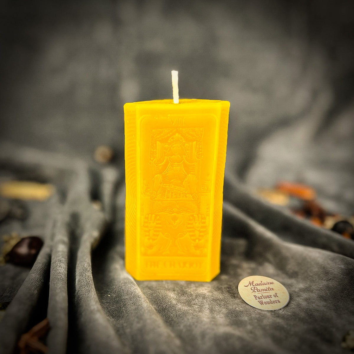 Golden yellow beeswax The Chariot tarot card candle standing on gray cloth