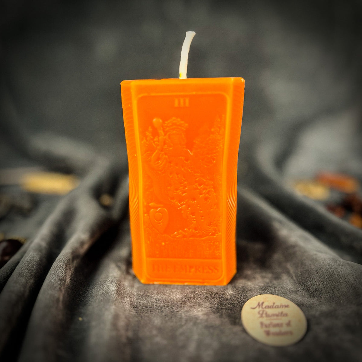 Bright orange beeswax The Empress tarot card candle standing on draped gray fabric