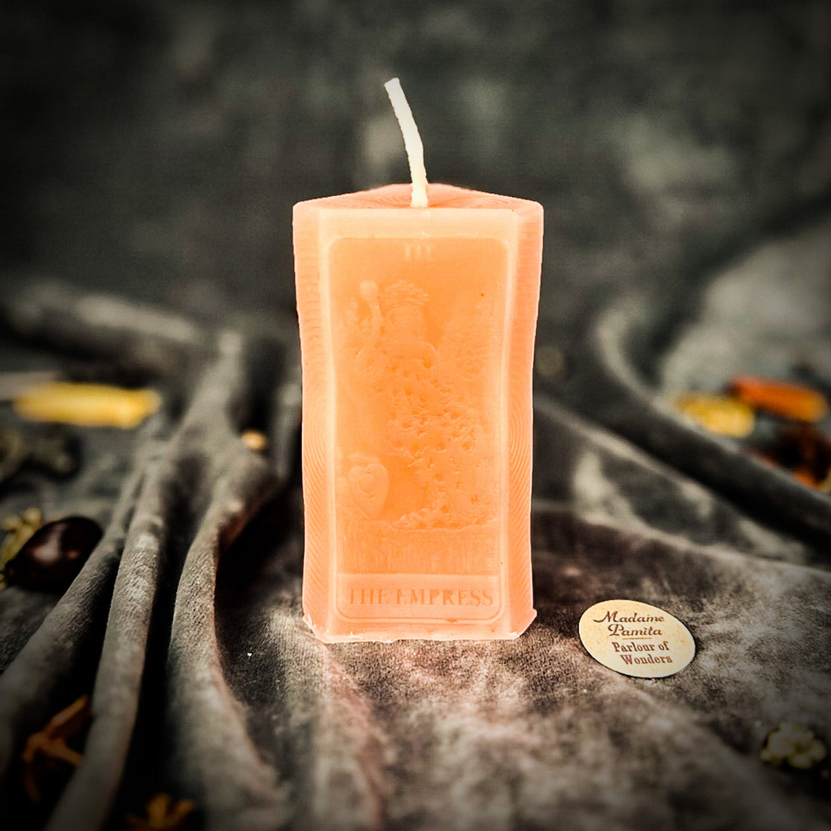 Pale peach beeswax The Empress tarot card candle on gray draped cloth