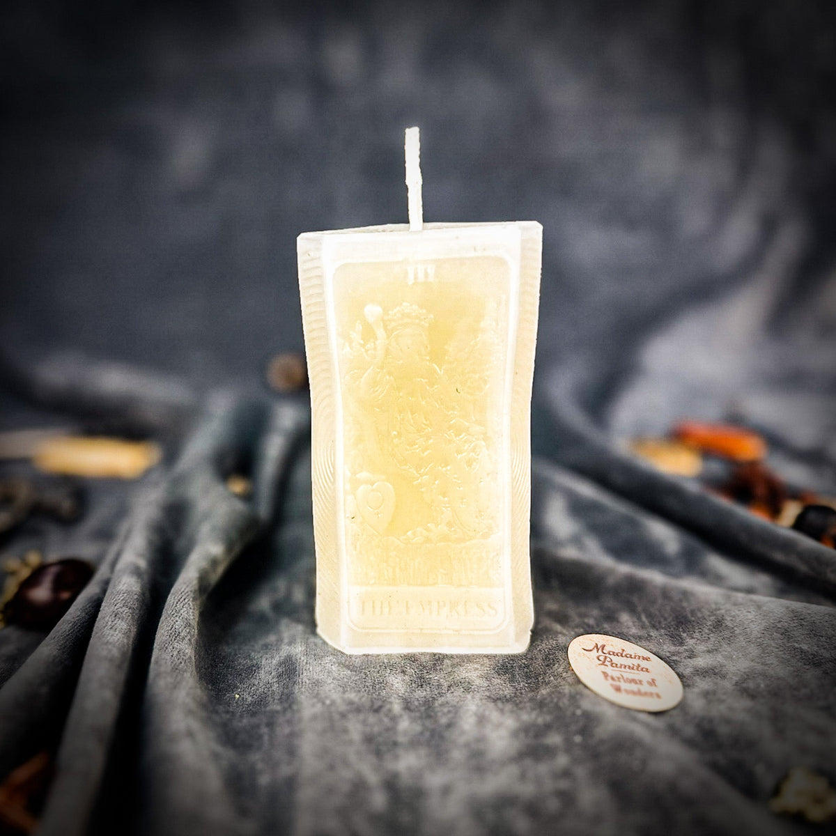 Cream white beeswax The Empress tarot card candle standing on gray fabric