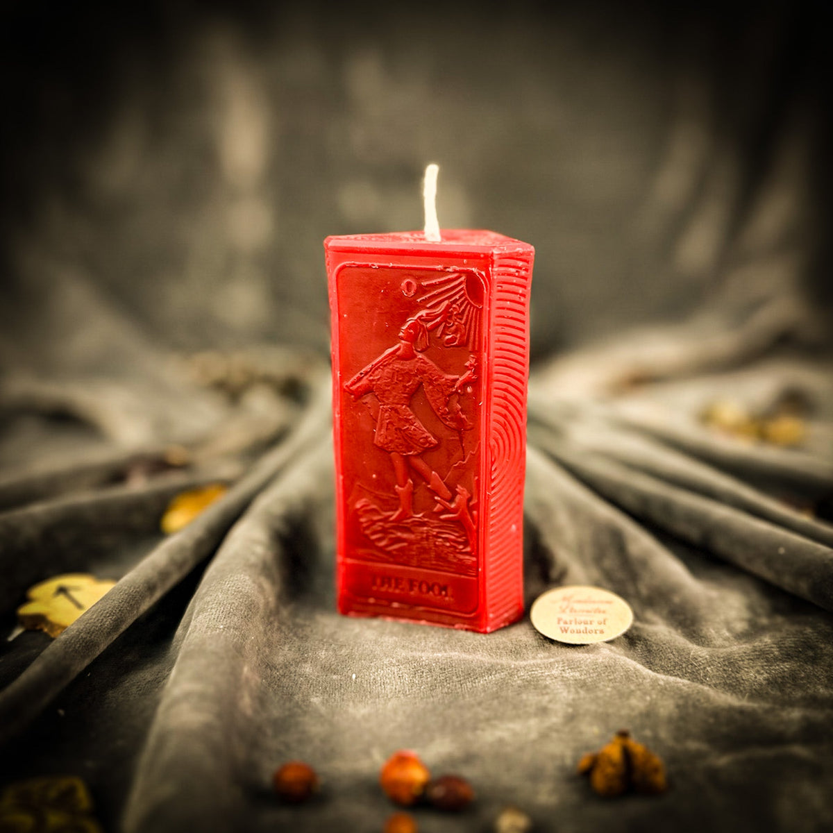 The Fool beeswax tarot candle in red on draped gray fabric