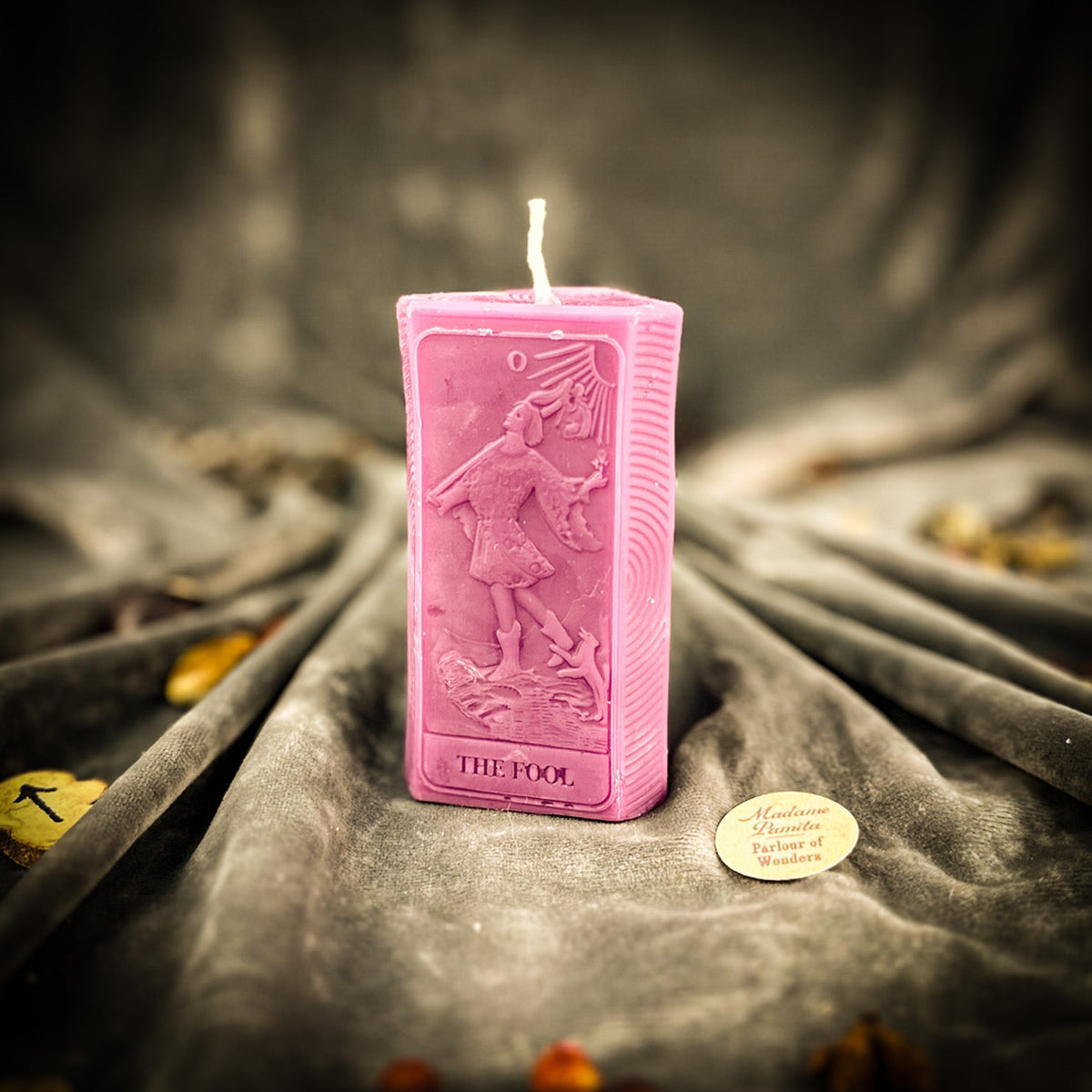 The Fool beeswax tarot candle in pink on draped gray fabric