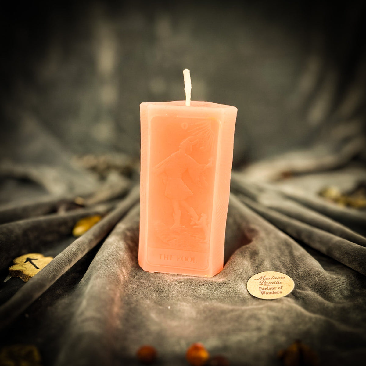 The Fool beeswax tarot candle in peach pink on draped gray fabric