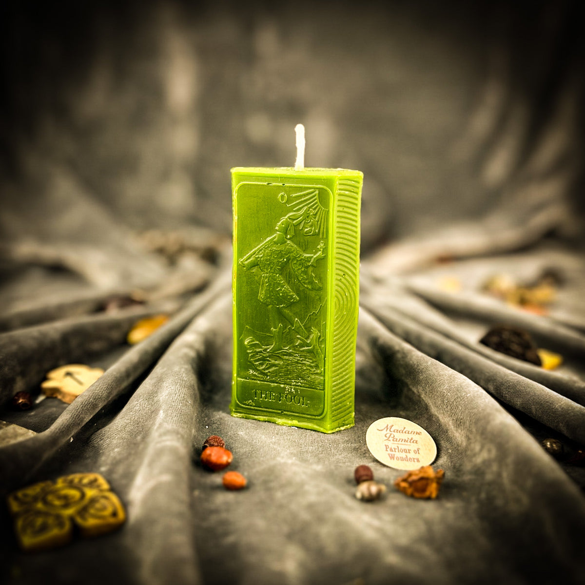 The Fool beeswax tarot candle in green on draped gray fabric