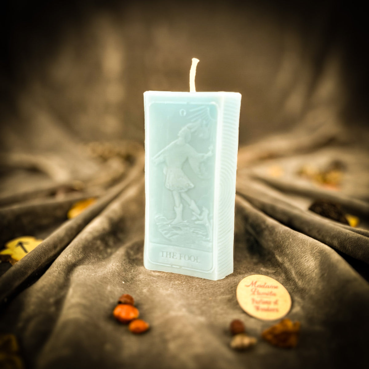 The Fool beeswax tarot candle in pale blue on draped gray fabric