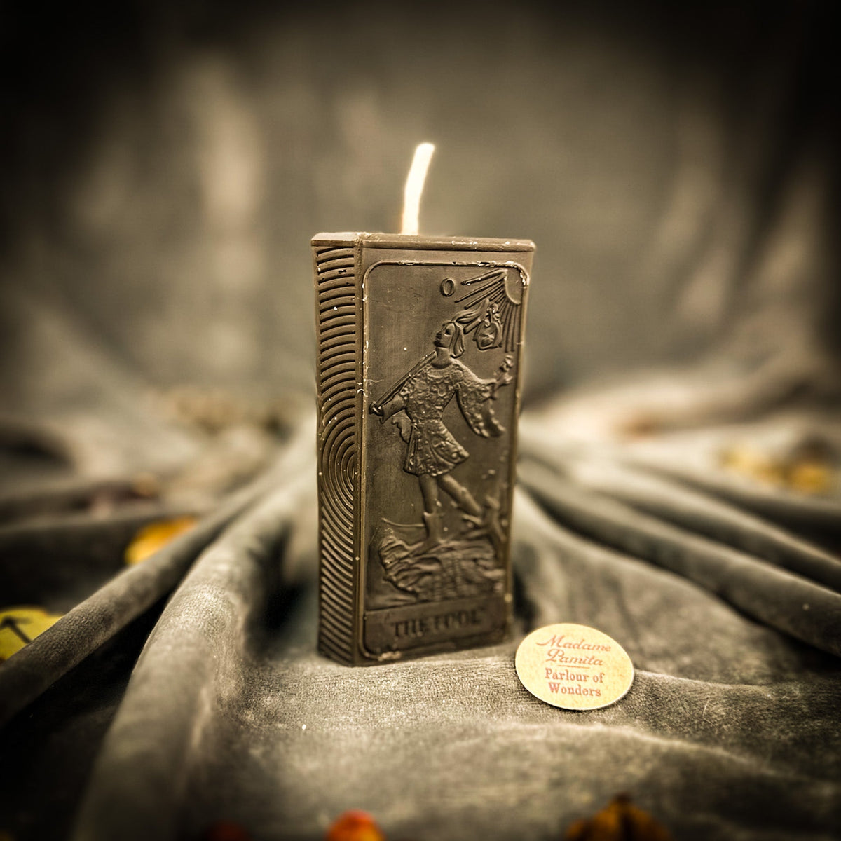 The Fool beeswax tarot candle in dark brown on draped gray fabric