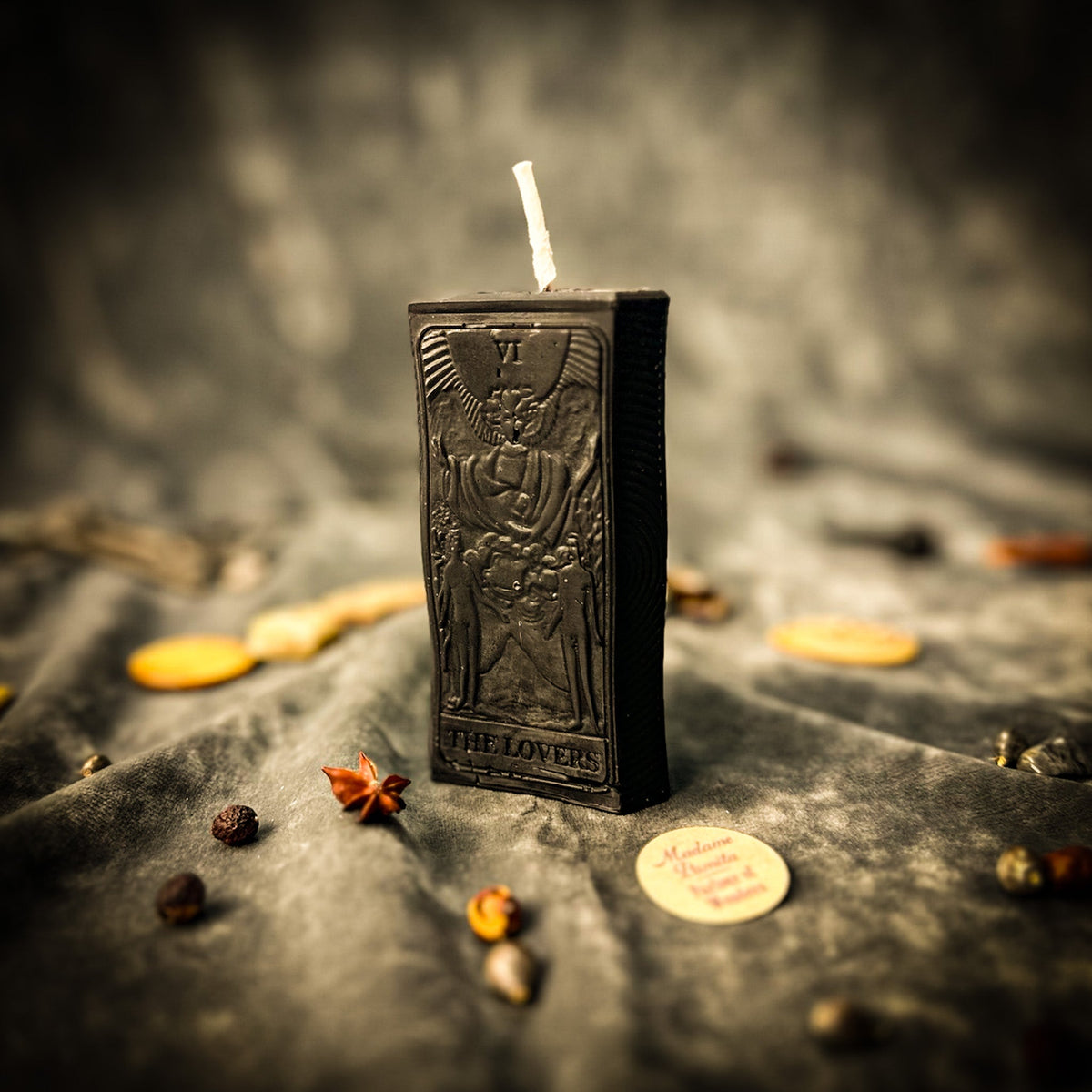 Black beeswax The Lovers tarot card candle on gray cloth with dried botanicals