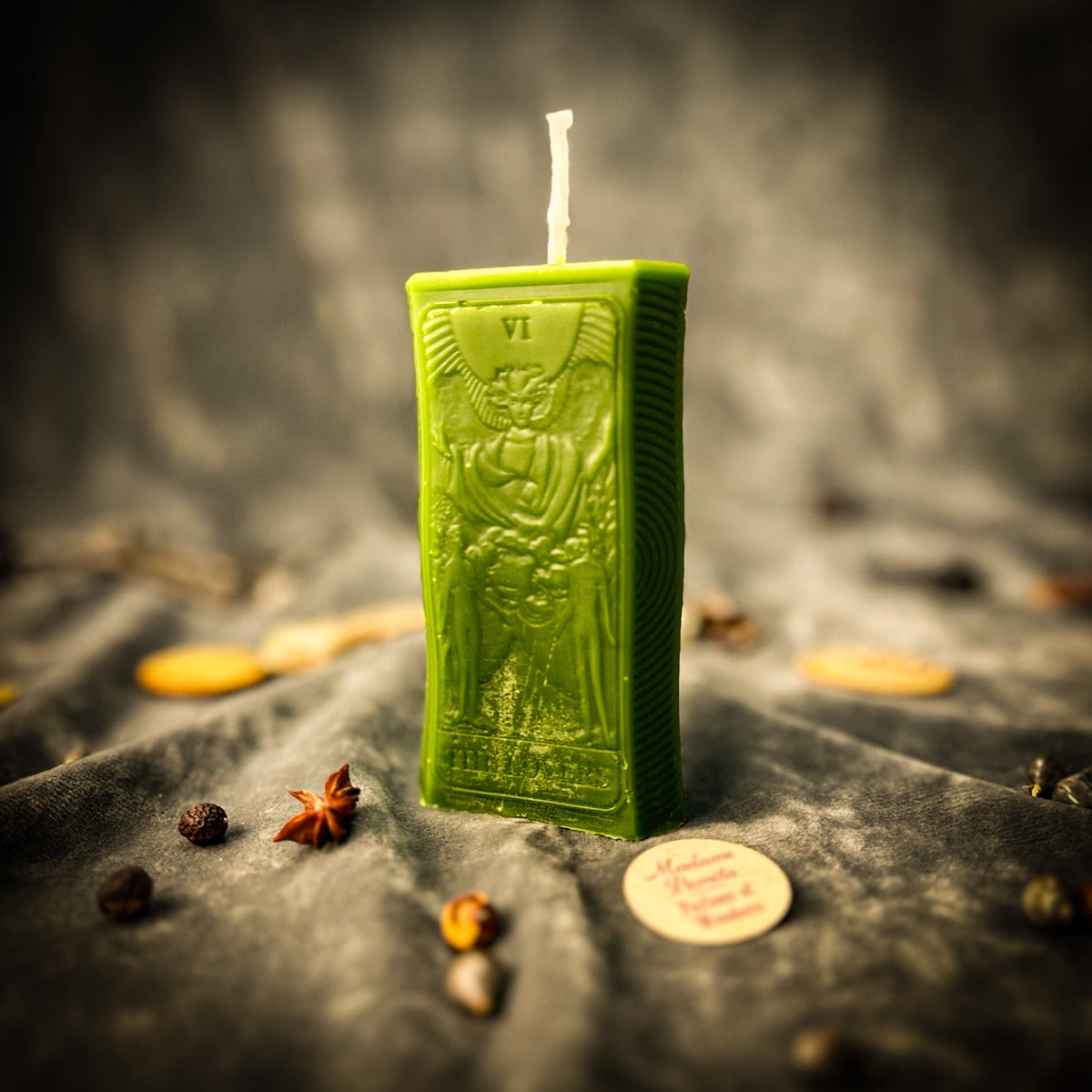 Olive green beeswax The Lovers tarot card candle standing on draped gray fabric