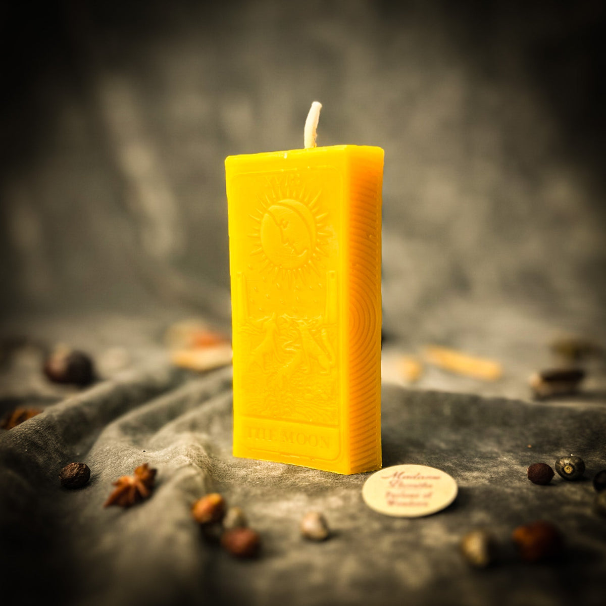 Golden yellow beeswax The Moon tarot card candle standing on gray draped cloth