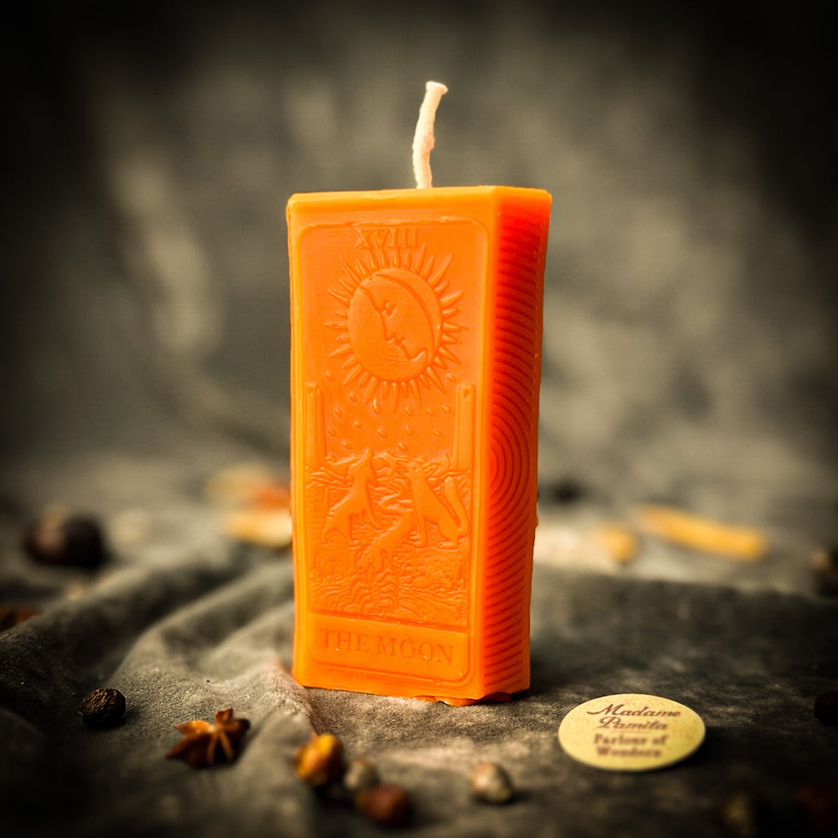 Bright orange beeswax The Moon tarot card candle on gray cloth
