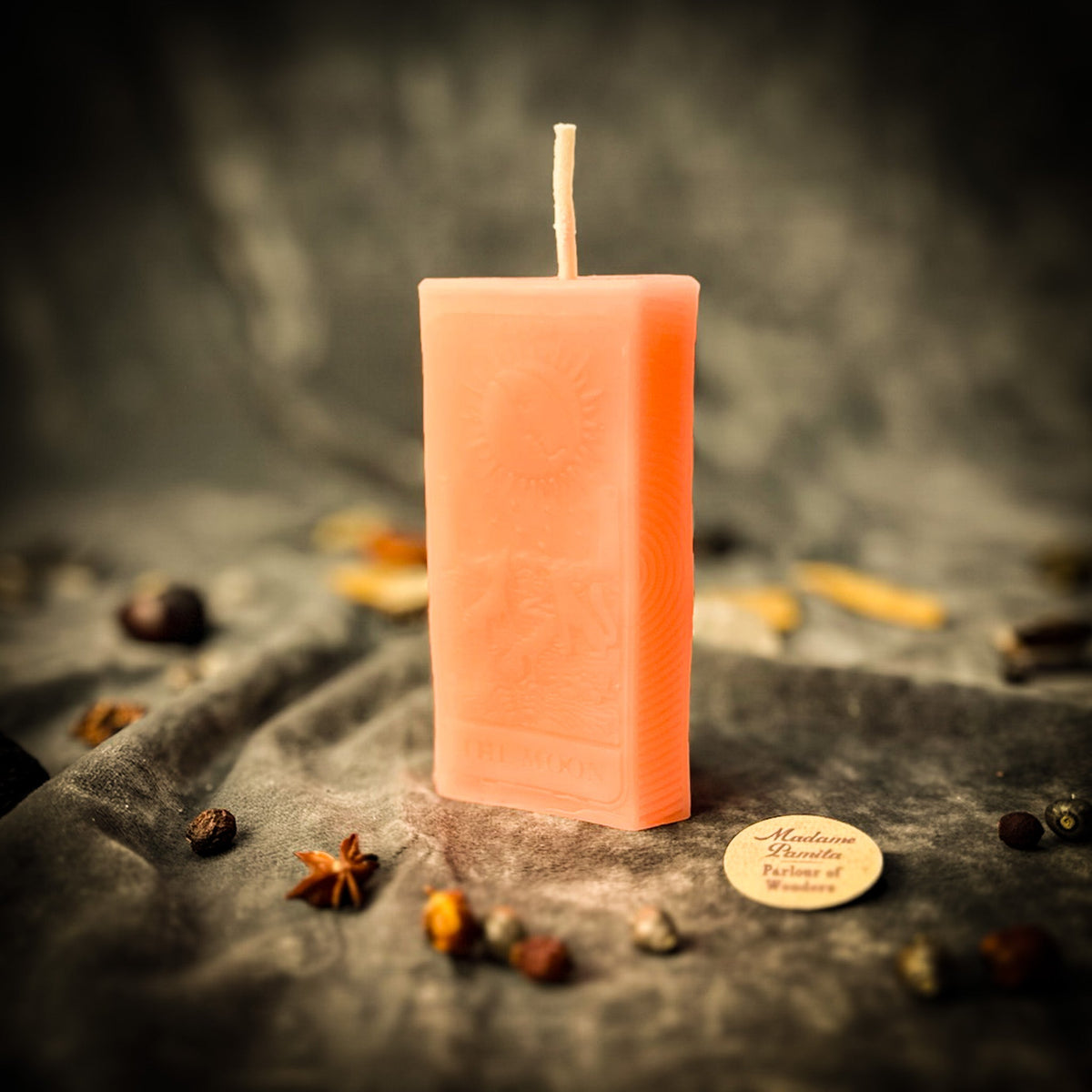 Pale peach beeswax The Moon tarot card candle among scattered dried botanicals