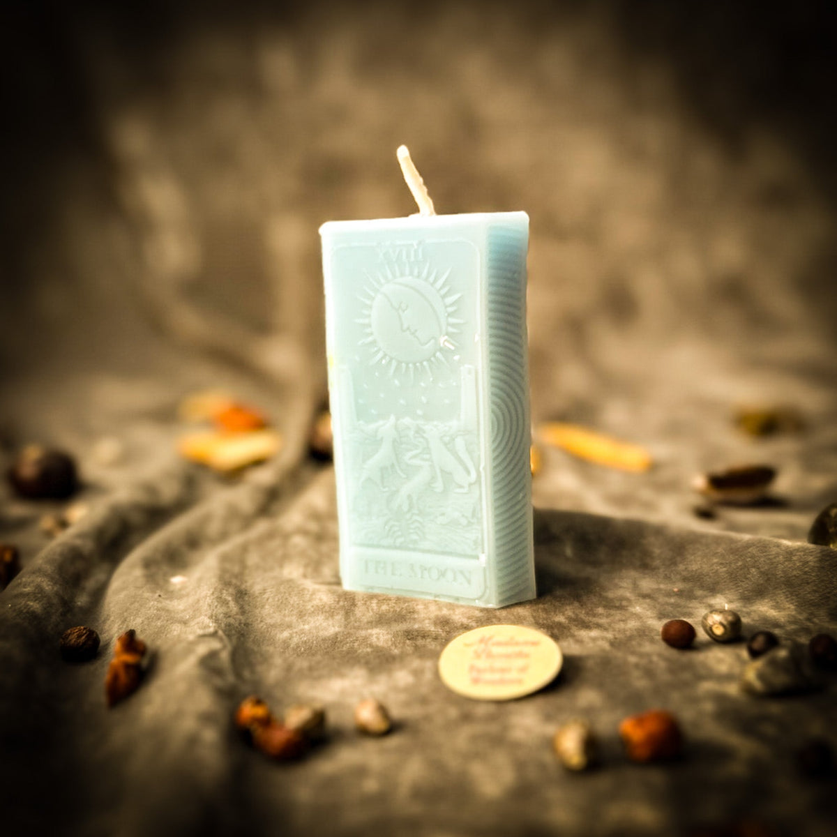 Pale blue beeswax The Moon tarot card candle standing on draped gray fabric
