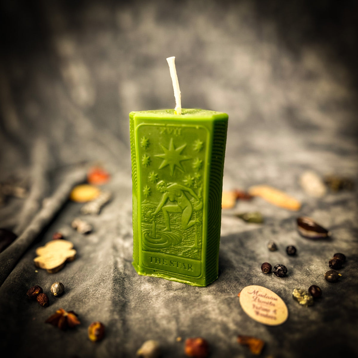 Olive green beeswax The Star tarot card candle standing on draped gray fabric