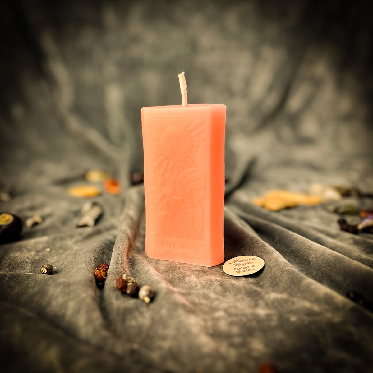 The Sun beeswax tarot candle in peach pink on draped gray fabric