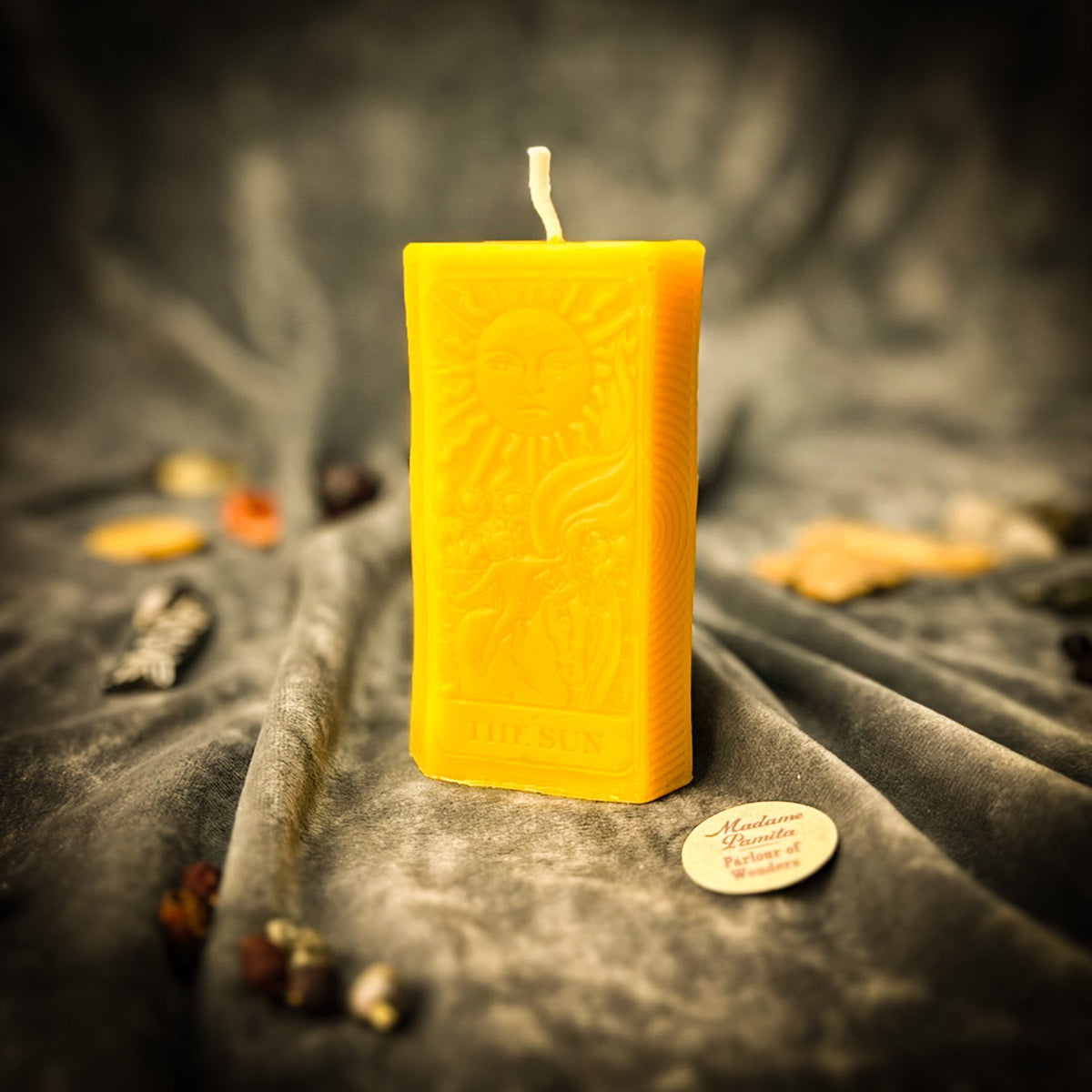 The Sun beeswax tarot candle in yellow on draped gray fabric