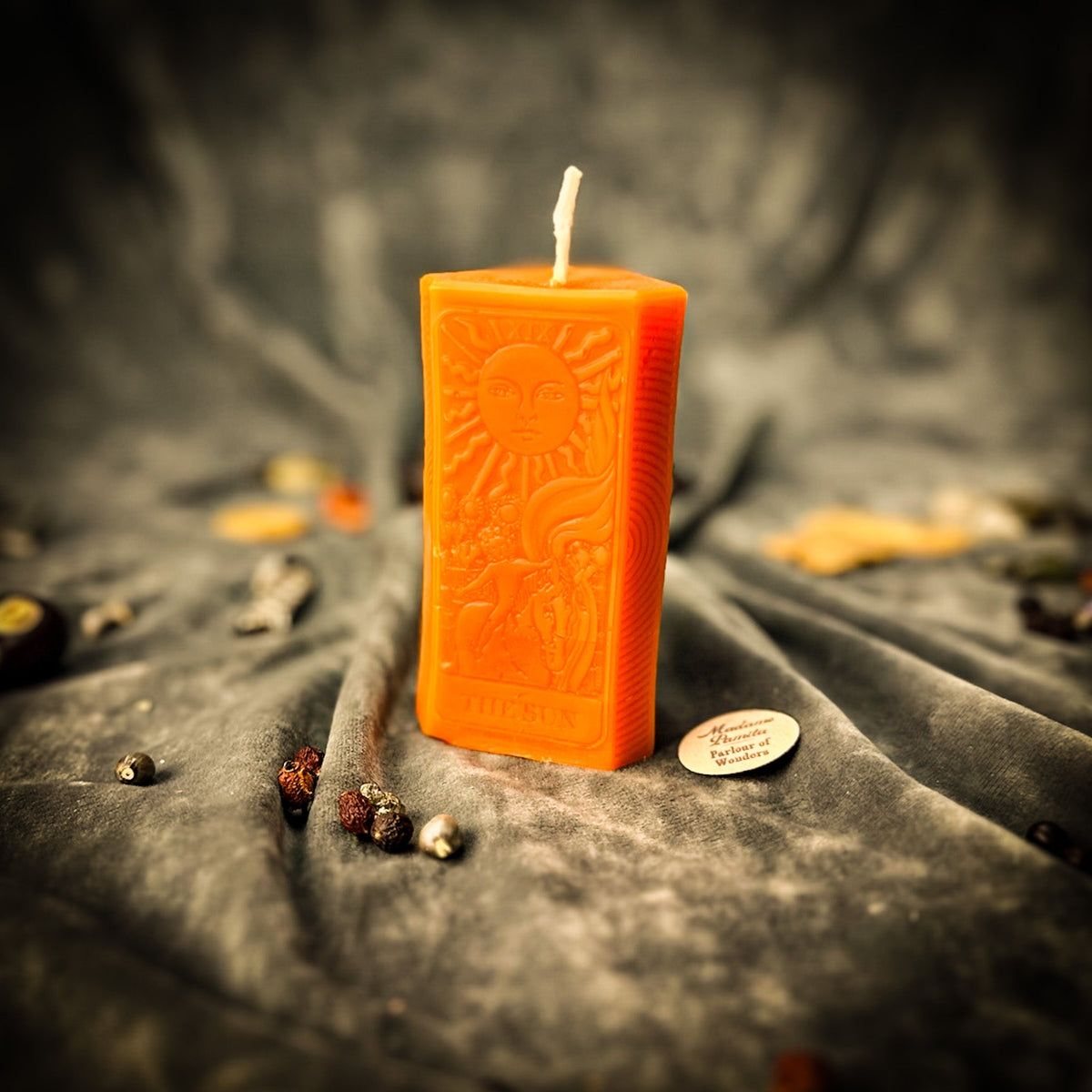 The Sun beeswax tarot candle in orange on draped gray fabric