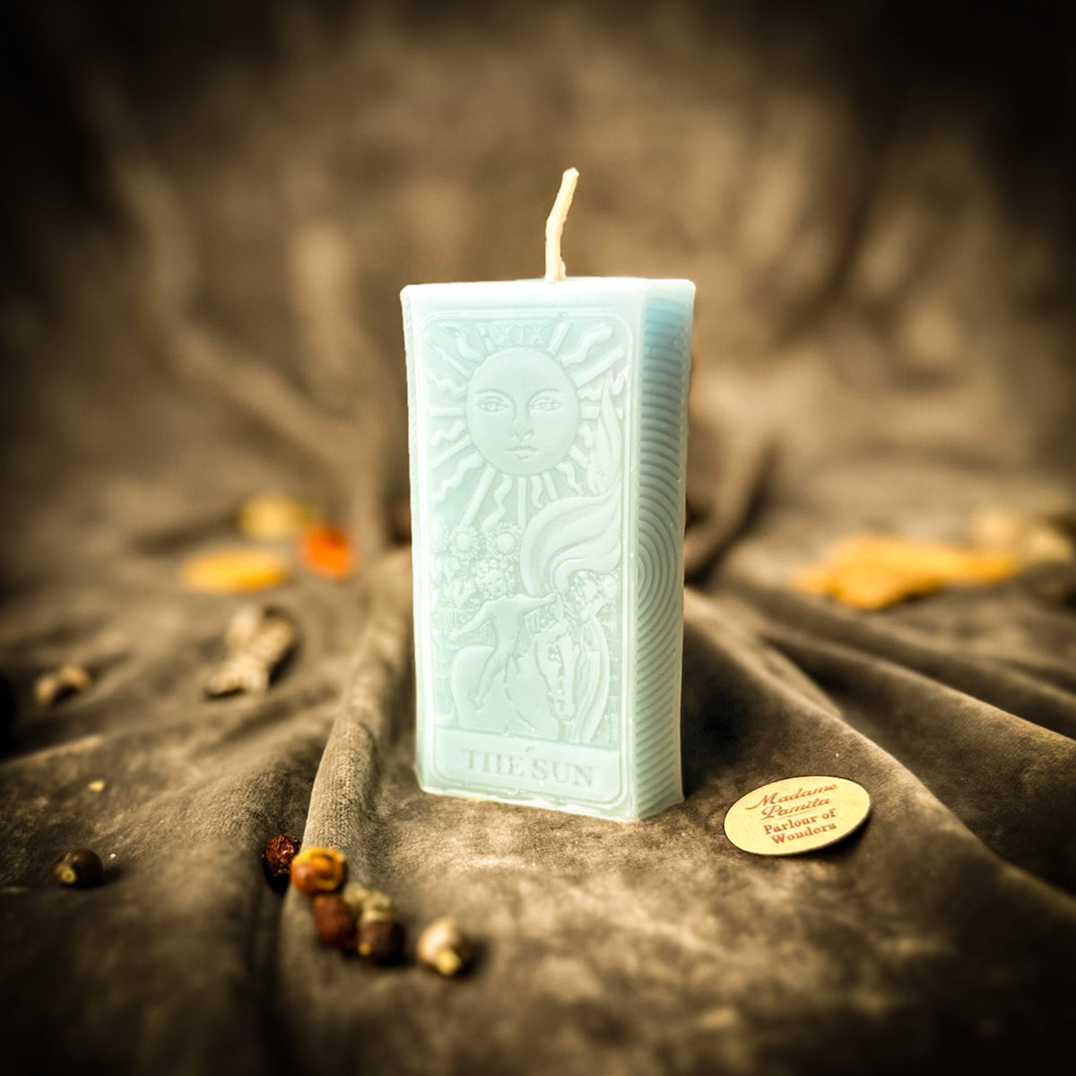 The Sun beeswax tarot candle in pale blue on draped gray fabric