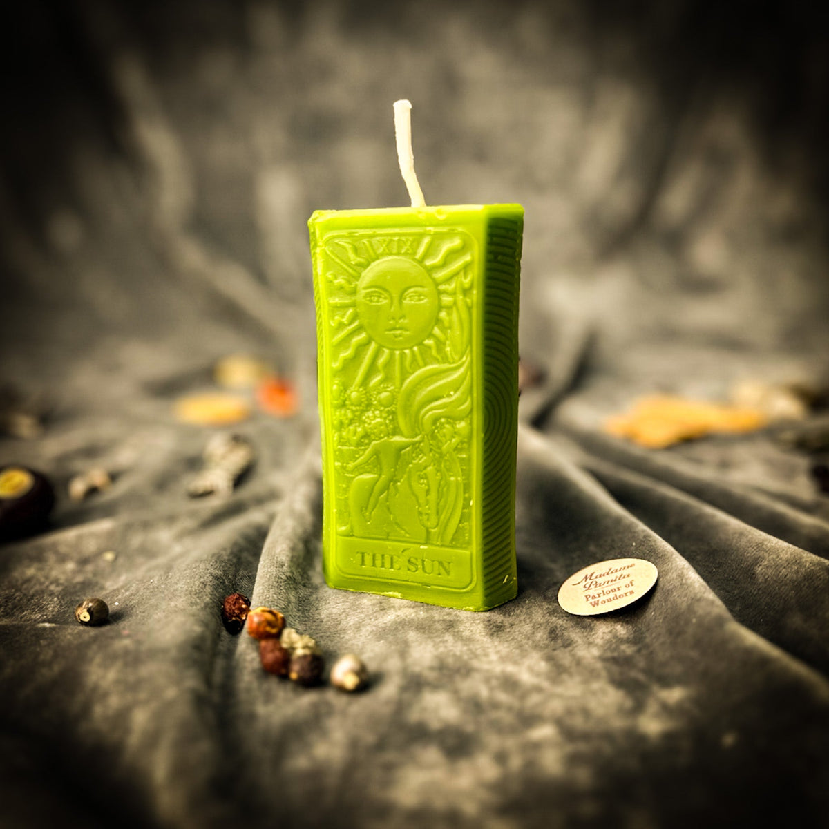 The Sun beeswax tarot candle in green on draped gray fabric