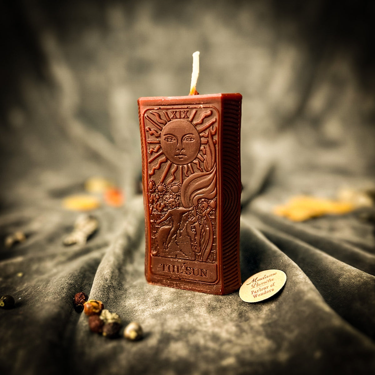 The Sun beeswax tarot candle in brown on draped gray fabric