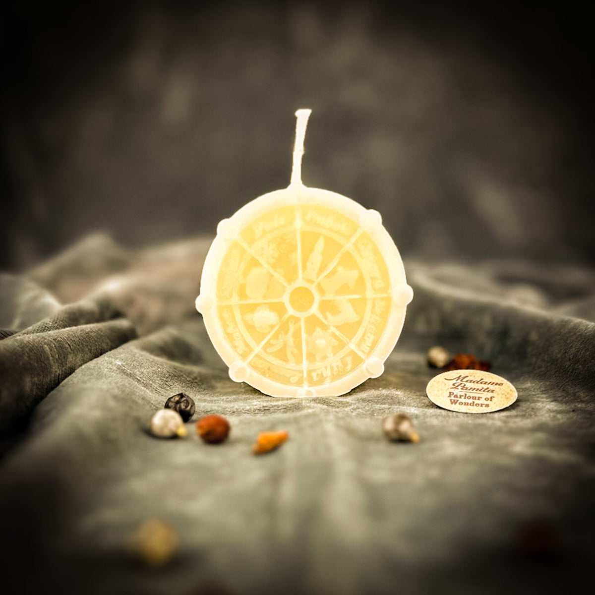 Cream-white Wheel of the Year candle, the spoked wheel and sabbat symbols soft in the pale wax.