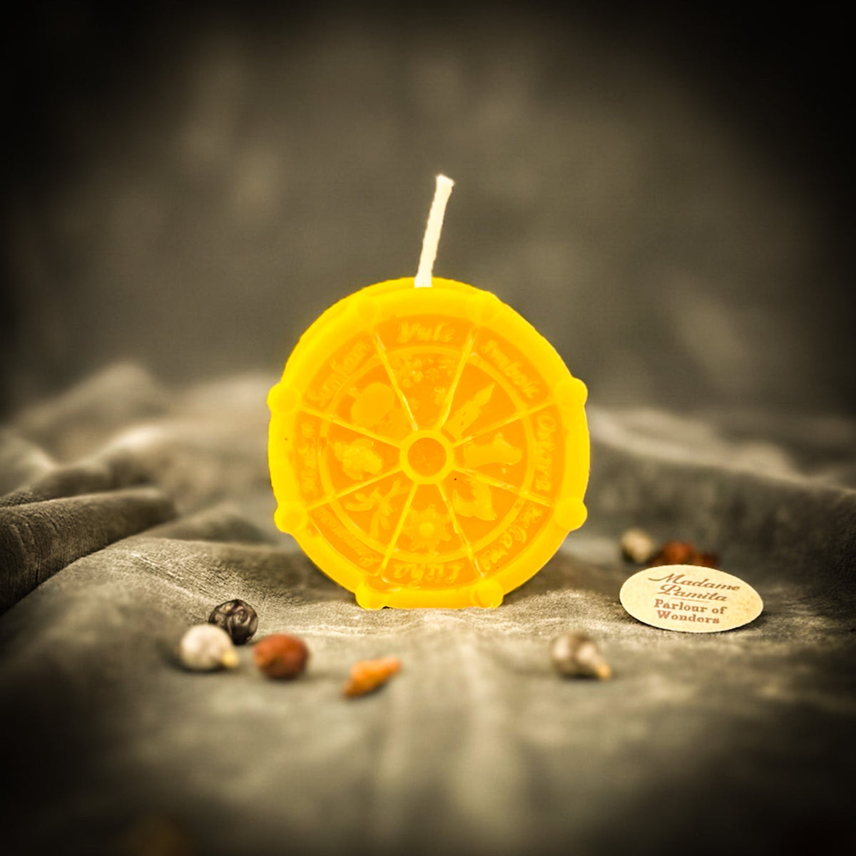 Golden-yellow Wheel of the Year candle standing on gray velvet with curios scattered in front.