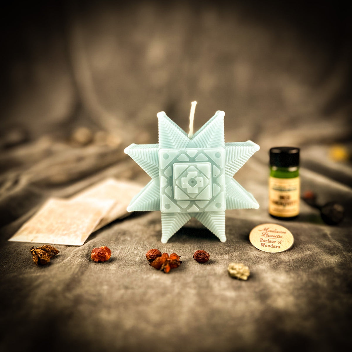 The kit in seafoam green: pale star candle with the oil bottle, printed instructions and scattered herbs on gray velvet