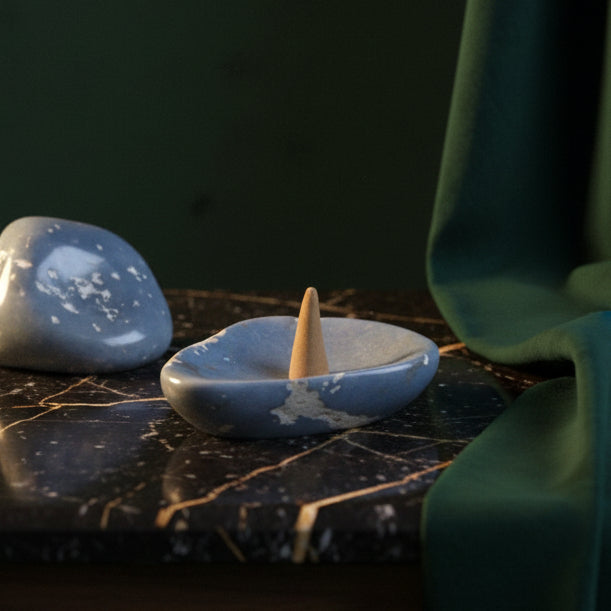 Blue angelite catchall on black marble holding a carved stone cone, raw angelite beside it
