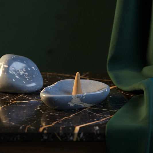 Blue angelite catchall on black marble holding a carved stone cone, raw angelite beside it