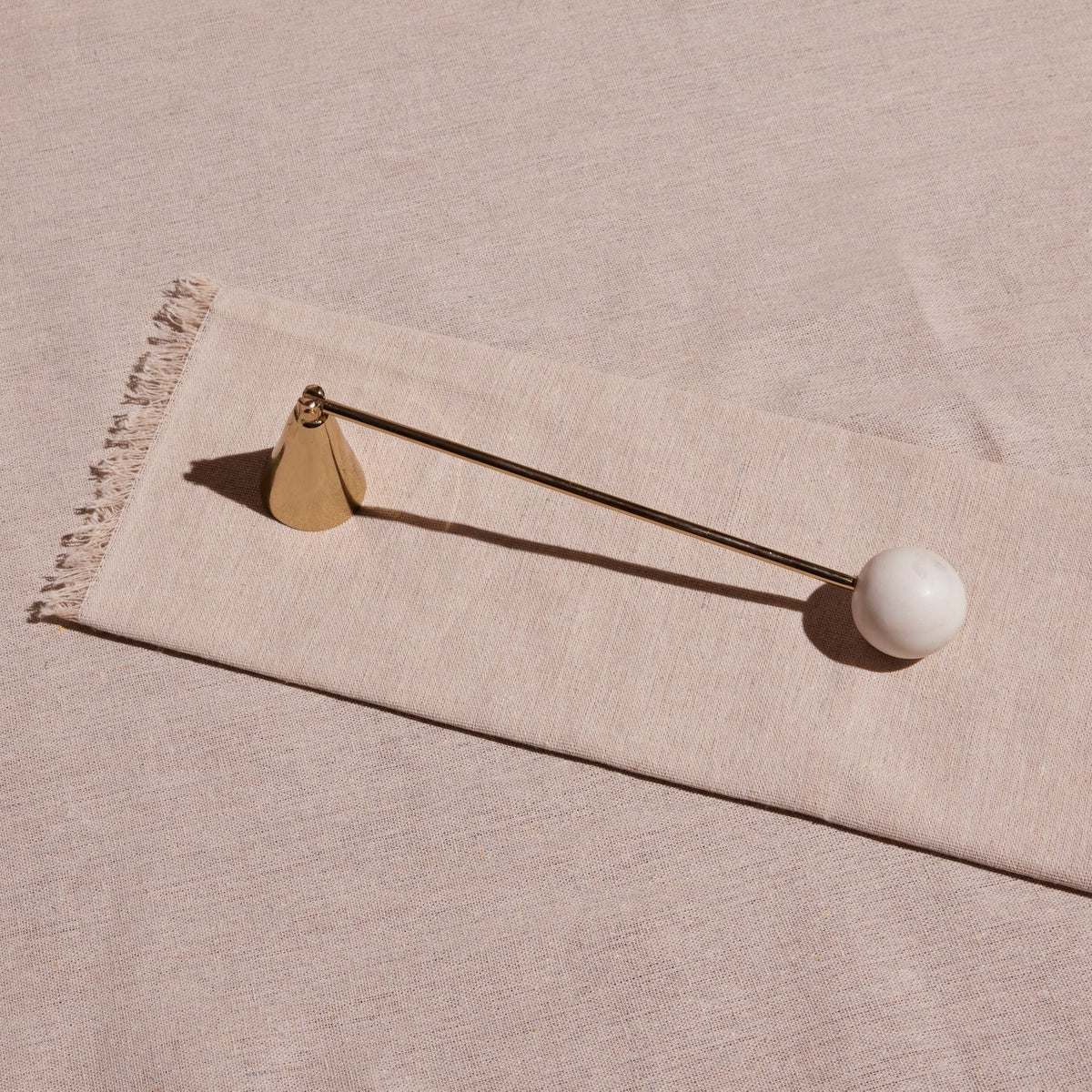 Anka candle snuffer seen from above on pale linen, showing the brass bell and marble handle